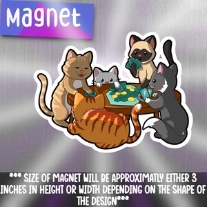 May include: Four cartoon cats playing a board game with green hexagonal tiles. The cats are orange, gray, white, and black. The game is on a wooden table. The magnet is approximately 3 inches in height or width.