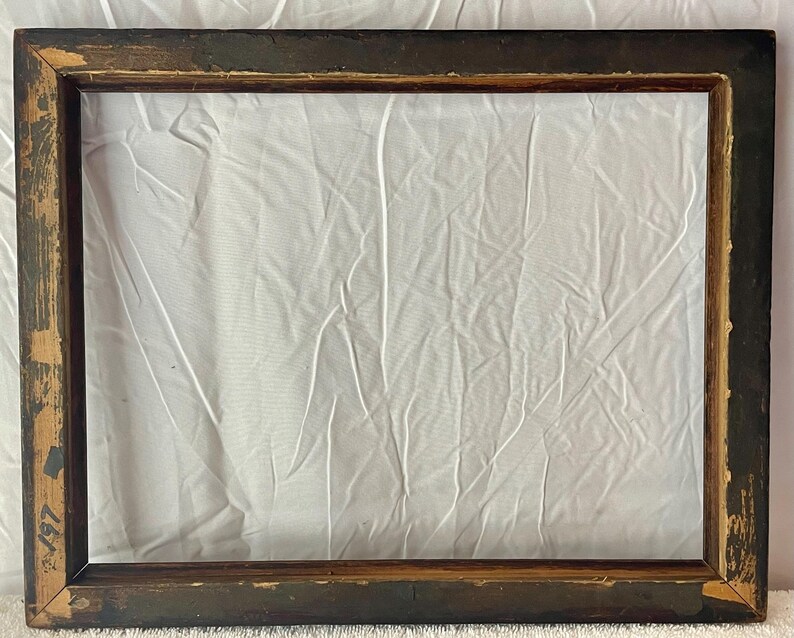May include: Rectangular wooden picture frame with a dark brown exterior and a lighter brown interior. The frame has visible signs of wear, with some paint chipping off, revealing the wood underneath. The frame is empty, with a white fabric background.
