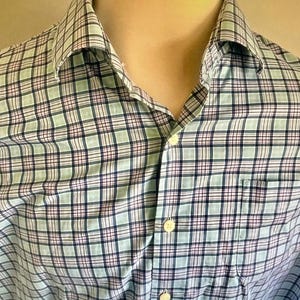 May include: A button-down shirt with a plaid pattern in shades of light blue, white, navy, and red. The shirt has a collar, a chest pocket, and white buttons. The fabric appears to be a lightweight cotton or blend.