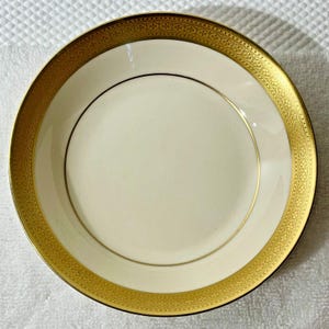 May include: A white ceramic saucer with a gold rim and intricate floral pattern. The saucer has a smooth, glossy finish.