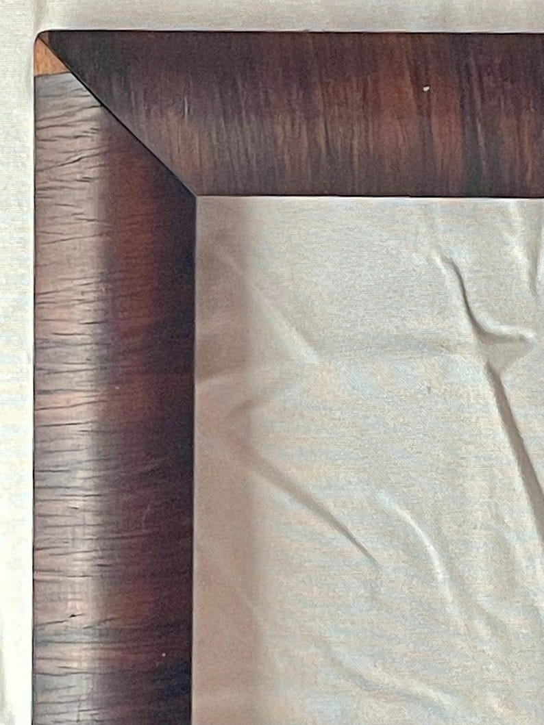 May include: Close-up of a wooden frame corner. The frame has a dark brown, textured finish with visible wood grain. The corner is a precise 90-degree angle. A light-colored, possibly fabric, surface fills the interior space.