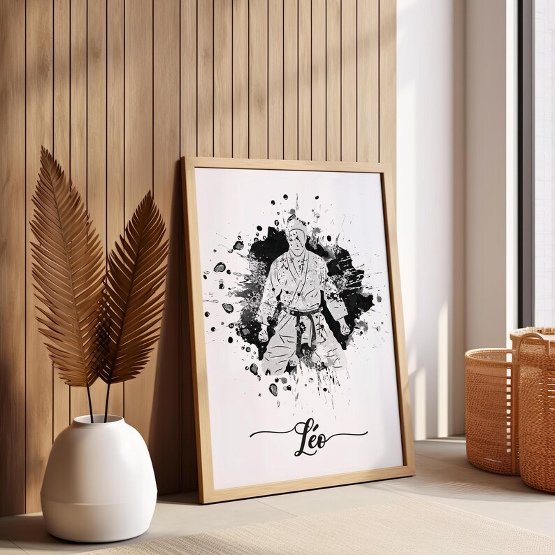 May include: Black and white watercolor illustration of a person in a karate uniform with a white belt. The illustration is surrounded by black splatters of paint. The name "Leo" is written in cursive at the bottom of the image.
