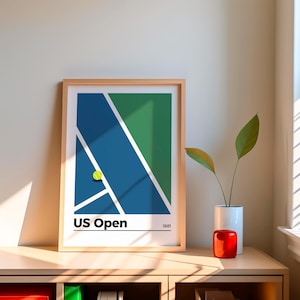 May include: A framed print of a minimalist design depicting a tennis court with a green and blue color scheme. The print includes the text "US Open" and the year "1881".