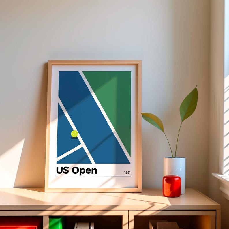 May include: A framed print of a minimalist design depicting a tennis court with a green and blue color scheme. The print includes the text "US Open" and the year "1881".