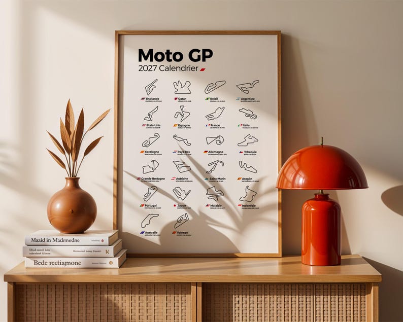 K&ouml;nnte beinhalten: Ein gerahmtes Wandposter mit dem Titel Moto GP 2027 Calendrier, das ein Raster aus schwarzen Linienzeichnungen von Rennstrecken mit L&auml;ndernamen und Flaggen zeigt. Es steht auf einem Holzm&ouml;bel neben drei B&uuml;chern, einer braunen Vase und einer roten Lampe.