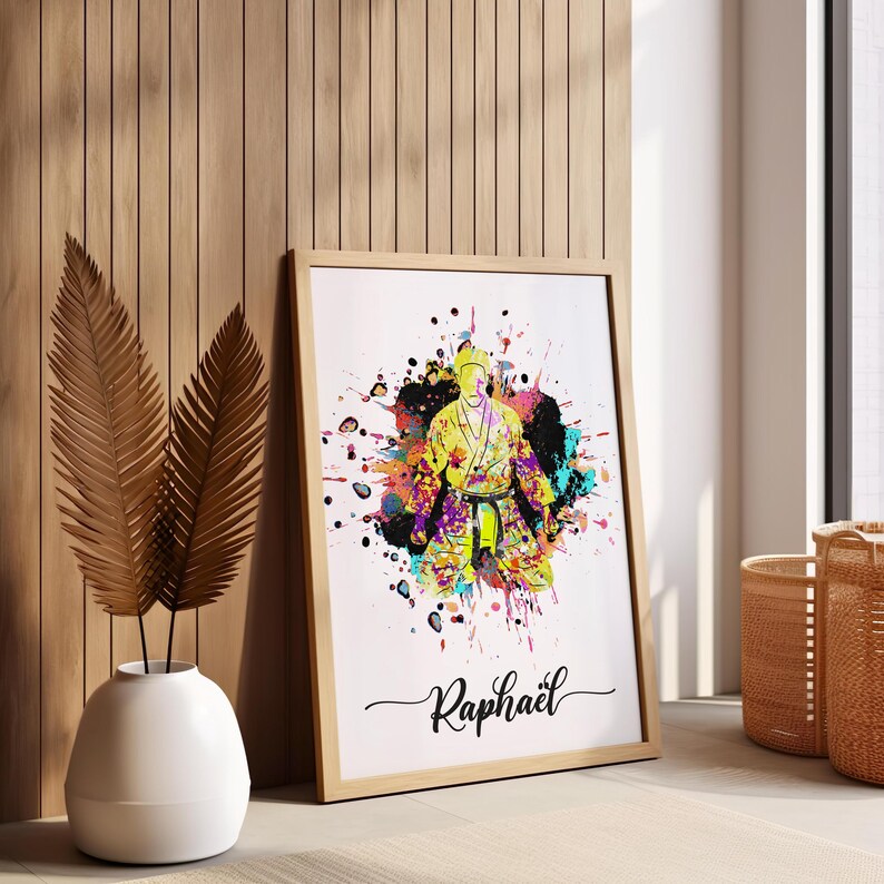 May include: A colorful watercolor print of a person in a yellow martial arts uniform with a black belt. The print is surrounded by colorful paint splatters and the name "Raphael" is written in cursive at the bottom.