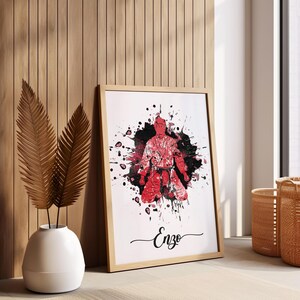May include: A framed print with a red and black watercolor illustration of a person in a karate pose. The background is white with black splatters of paint. The name "Enzo" is written in cursive at the bottom of the print.