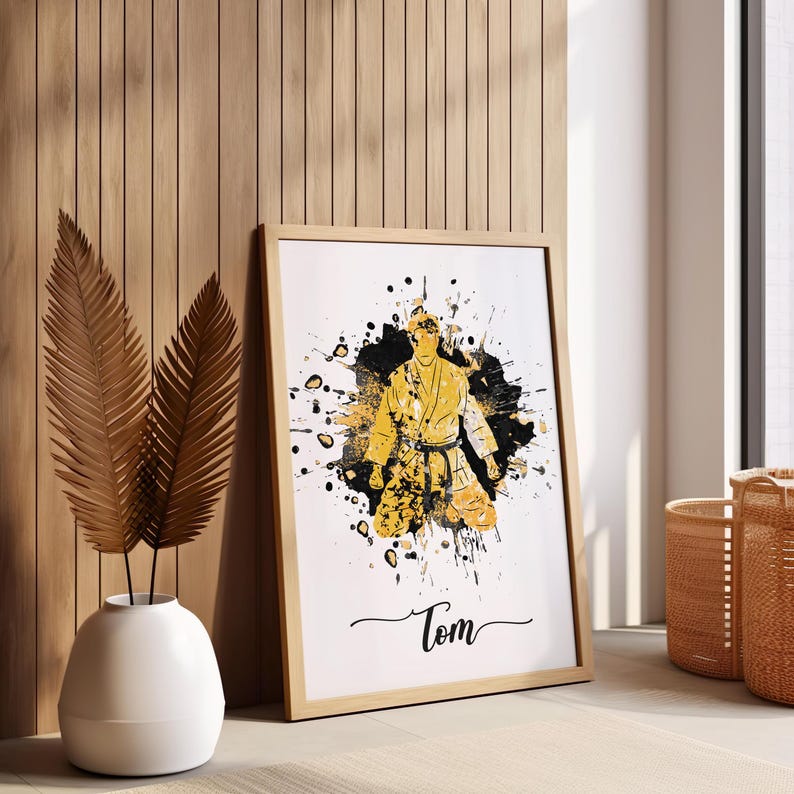 May include: A framed print of a person in a yellow karate uniform with black belt, standing in a black and white splatter paint design. The print has the name "Tom" written at the bottom.