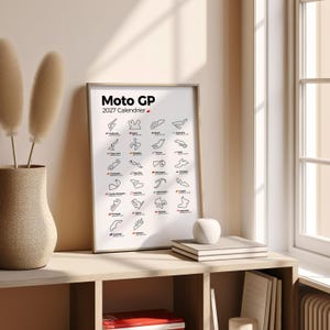 K&ouml;nnte beinhalten: Ein gerahmtes wei&szlig;es Poster mit dem Titel Moto GP 2027 Calendrier, das ein Raster aus schwarzen Linienzeichnungen verschiedener internationaler Rennstrecken zeigt, wobei jede mit dem L&auml;ndernamen und Ort in kleiner schwarzer Schrift beschriftet ist.