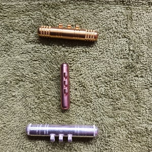 Puede incluir: Tres juguetes de fidget de metal, uno dorado, uno plateado y uno de cobre, sobre una superficie verde texturizada.