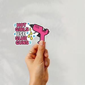May include: A pink glue gun sticker with the text "HOT GIRLS USE GLUE GUNS" in pink and blue. The sticker has a white border and is decorated with blue hearts and yellow teardrops.