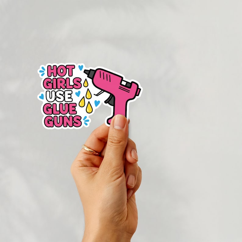 May include: A pink glue gun sticker with the text "HOT GIRLS USE GLUE GUNS" in pink and blue. The sticker has a white border and is decorated with blue hearts and yellow teardrops.