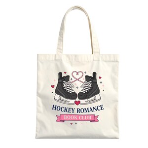 Puede incluir: Bolso tote color crema con un dise&ntilde;o de dos patines de hielo negros con cordones blancos y un coraz&oacute;n rosa. El texto "HOCKEY ROMANCE BOOK CLUB" est&aacute; en una pancarta rosa debajo de los patines, con peque&ntilde;os corazones y estrellas.
