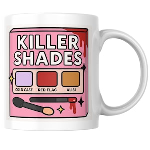 May include: White ceramic mug featuring a pink graphic with the text "KILLER SHADES." The graphic includes a makeup palette with three color swatches labeled "COLD CASE," "RED FLAG," and "ALIBI." Makeup brushes and star accents complete the design.