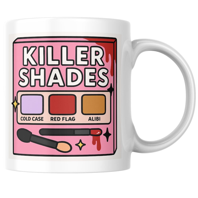 May include: White ceramic mug featuring a pink graphic with the text "KILLER SHADES." The graphic includes a makeup palette with three color swatches labeled "COLD CASE," "RED FLAG," and "ALIBI." Makeup brushes and star accents complete the design.