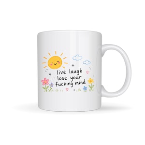 Puede incluir: Taza de cer&aacute;mica blanca con un dise&ntilde;o caprichoso. La taza presenta un sol sonriente, nubes, flores y el texto "live laugh lose your fucking mind". La taza tiene un asa curvada.