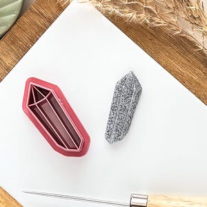 May include: Two crystal-shaped cookie cutters, one pink and one grey, on a white surface.
