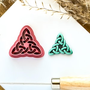 May include: A set of two triangle-shaped cookie cutters. One is pink and the other is teal. Both feature a Celtic knot design.