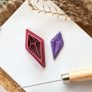 May include: Two diamond-shaped cookie cutters, one red and one purple, with a wooden-handled tool for decorating cookies.