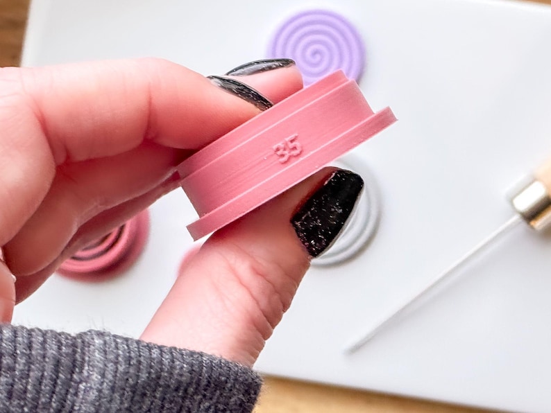 May include: Pink plastic cookie cutter with a spiral design and the number 35 printed on it.