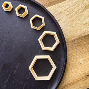 May include: A set of five wooden hexagon-shaped cookie cutters of varying sizes on a black tray. The cookie cutters are arranged in a semi-circle.