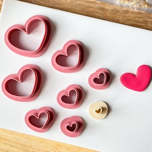 May include: A set of seven pink heart-shaped cookie cutters of varying sizes, with one larger solid pink heart.