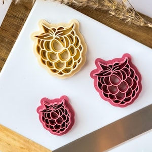 May include: Three cookie cutters in the shape of raspberries. One is yellow, and two are pink.