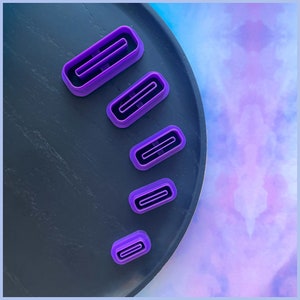 May include: Five purple plastic cookie cutters in different sizes, arranged in a row on a black surface.