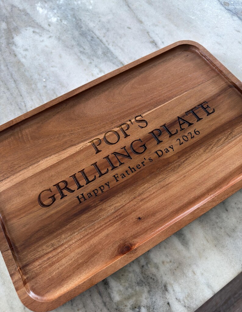 May include: A rectangular wooden serving tray with rounded corners and a natural grain finish. The surface is laser-engraved with the text POP'S GRILLING PLATE and the inscription Happy Father's Day 2026 in a dark, clear, sans-serif font.