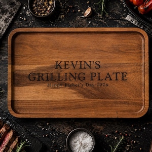 May include: A rectangular wooden serving tray with rounded corners and a raised edge. The center is engraved with the text KEVIN'S GRILLING PLATE and Happy Father's Day 2026 in a dark, sans-serif font, showcasing the natural brown wood grain.