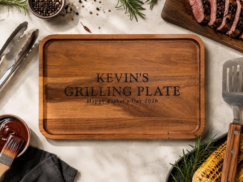 May include: A rectangular wooden serving tray with rounded corners and a grooved border. The center is engraved with the text KEVIN'S GRILLING PLATE and Happy Father's Day 2026 in a dark, serif font, showcasing the natural brown wood grain.