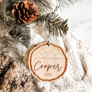 May include: A wooden Christmas ornament with a mountain scene and the text "My First Christmas Cooper 2023".