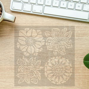 May include: A stencil with four floral designs. The designs are intricate and detailed, with a white outline on a clear background.