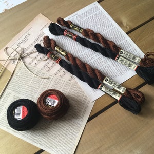 May include: Four spools of embroidery floss, two black and two brown, with labels that read "310 898" and "51". Two balls of embroidery floss, one black and one brown, with labels that read "310 898" and "DM 898".