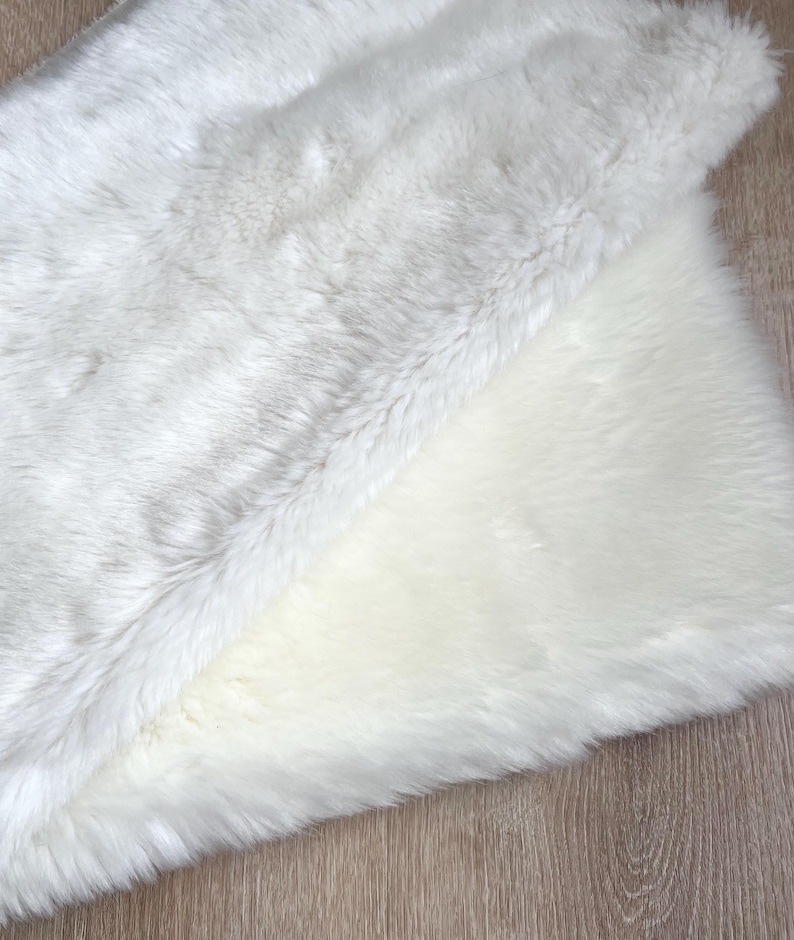 May include: A white faux fur rug with a soft, fluffy texture. The rug is folded in half, showing the underside of the fur.