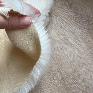 May include: Close-up of a beige fabric with a white faux fur trim. The fabric is soft and plush, and the fur is fluffy and luxurious.