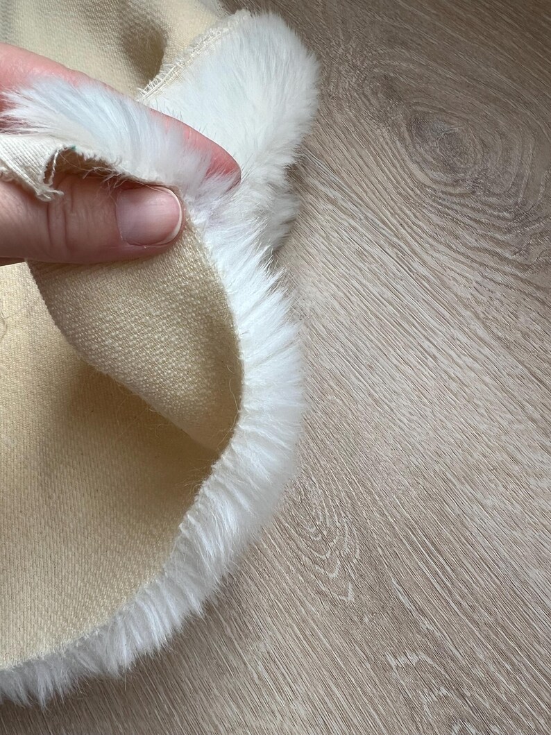 May include: Close-up of a beige fabric with a white faux fur trim. The fabric is soft and plush, and the fur is fluffy and luxurious.