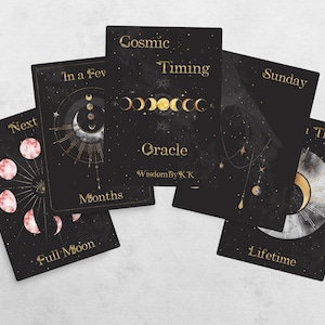 May include: Black oracle cards with gold celestial designs and text. The cards feature phases of the moon, stars, and phrases like "Cosmic Timing Oracle" and "Full Moon". The cards are arranged on a light background.