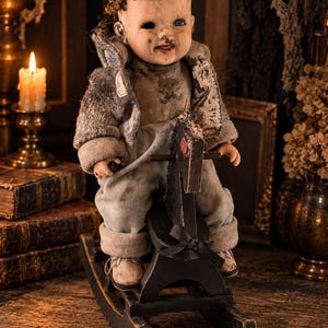 May include: A vintage doll with a weathered face, one missing eye, and dark textured hair, wearing a distressed grey jacket and matching trousers. The doll is seated on a small, black wooden rocking horse with a red accent on the head.
