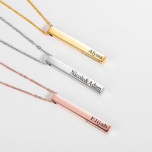 Peut inclure: Trois colliers à barre en or, argent et or rose avec des noms personnalisés gravés sur les barres. Le collier à barre en or a les noms "Alyssa" et "Samuel" gravés dessus. Le collier à barre en argent a les noms "Nicole & Adam" gravés dessus. Le collier à barre en or rose a les noms "Elijah" et "Jessica" gravés dessus.