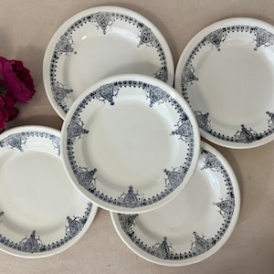 May include: Five white ceramic plates with a blue and white geometric pattern around the rim. The plates are stacked on top of each other.