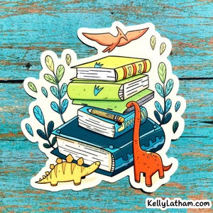 May include: A sticker featuring a stack of books with a pencil, dinosaurs, and a flying pterodactyl. The books are green and blue, with yellow and orange accents. The sticker has a white border and the text "KellyLatham.com STK103".