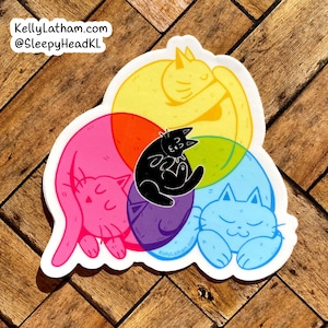 May include: A sticker featuring five cats in a circle, with each cat a different color: yellow, pink, purple, blue, and black. The cats are all curled up sleeping. The sticker has the text "KellyLatham.com" and "@SleepyHeadKL" on it.