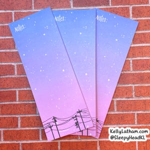 May include: Three pink and blue gradient notepad sets with the word "Notes" at the top of each page. The notepads feature a black silhouette of power lines against a starry night sky.