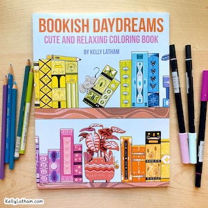 May include: A coloring book titled "Bookish Daydreams" with the subtitle "Cute and Relaxing Coloring Book" by Kelly Latham. The cover features illustrated bookshelves with colorful books, a mouse, and a potted plant. Colored pencils and markers are arranged around the book.