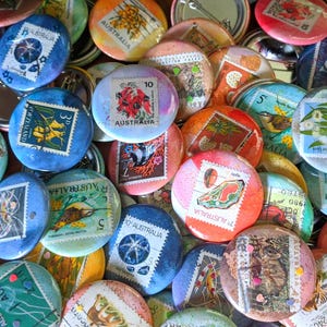 Può includere: Una collezione di bottoni rotondi colorati con francobolli australiani vintage. I bottoni sono decorati con immagini di uccelli, fiori e altri animali selvatici australiani. I bottoni sono un mix di blu, rosso, verde, giallo e arancione.