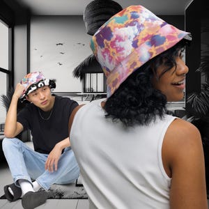 May include: Two people wearing bucket hats. One hat is black and white with a tie-dye pattern. The other hat is a colourful tie-dye pattern with pink, orange, yellow, and blue.