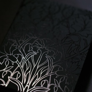 May include: A black notebook with a floral design. The design is a white, stylized illustration of flowers and leaves. The notebook is rectangular and appears to be made of a textured material.