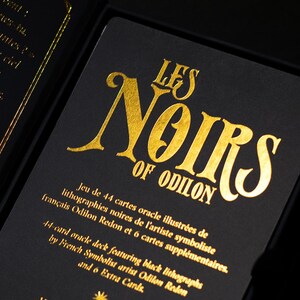 May include: A black oracle card deck with gold lettering. The text reads "LES NOIRS OF ODILON" and includes details about the 44-card deck featuring black lithographs by French Symbolist artist Odilon Redon.