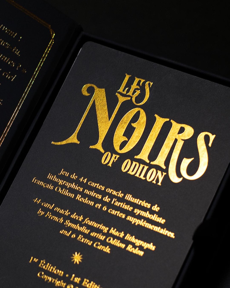 May include: A black oracle card deck with gold lettering. The text reads "LES NOIRS OF ODILON" and includes details about the 44-card deck featuring black lithographs by French Symbolist artist Odilon Redon.